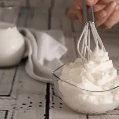 Ecco come fare la panna montata in casa: una ciotola di panna montata soffice, un frullino e una brocca di latte.