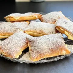 Deliziosi dolci con pasta sfoglia ripieni di crema e spolverati di zucchero a velo, serviti su un piatto di vetro.