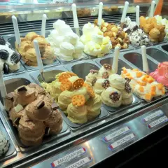 Vetrina piena di gusti di gelato, alcuni con panna montata e decorazioni golose.