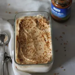 Gelato cremoso con granella di nocciole, accanto a un barattolo di dulce de leche.