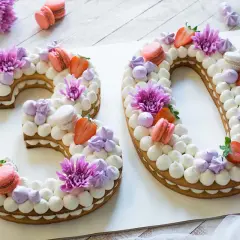 Torta numero 30 decorata con panna, fragole, macarons e fiori viola.