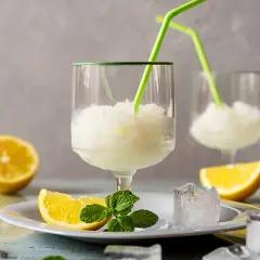 Sorbetto al limone fresco, preparato con la gelatiera, servito in bicchieri con cannucce verdi, guarnito con spicchi di limone e menta.