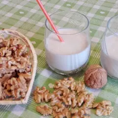Due bicchieri con latte di noci fatto in casa, una ciotola a forma di cuore piena di noci e noci sparse sul tavolo.