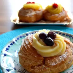Zeppole, deliziosi dolci napoletani, guarnite con crema pasticcera e frutti di bosco su un piatto decorato.