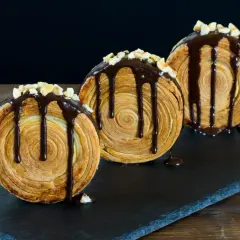 Tre deliziosi new york roll, ricoperti di cioccolato fuso e granella di nocciole, su una lavagna scura.