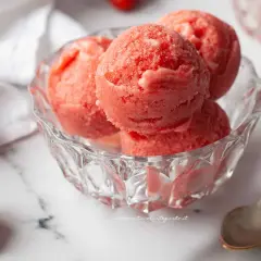 Coppa di sorbetto cremoso alle fragole, fresca e invitante, con fragole fresche e cucchiaini d'argento su sfondo marmorizzato.