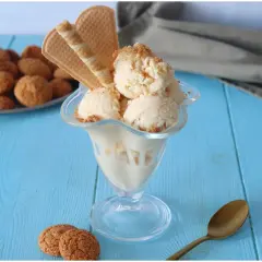 Coppa di gelato amaretto con biscotti e cialde su tavolo blu.