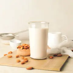 Un bicchiere di latte di mandorla fatto in casa, circondato da mandorle fresche su un tagliere di legno.