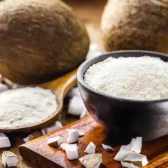 Cocco grattugiato in una ciotola e un cucchiaio, con noci di cocco intere e pezzi di cocco sullo sfondo. Ideale per sostituire la farina di cocco.