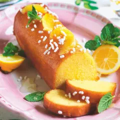 Una deliziosa torta al limone glassata, decorata con fette d'arancia, zuccherini e menta, servita su un piatto rosa con spicchi di limone.