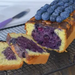 Plumcake ai mirtilli appena sfornato, con mirtilli freschi in cima e all'interno, su una griglia di raffreddamento.