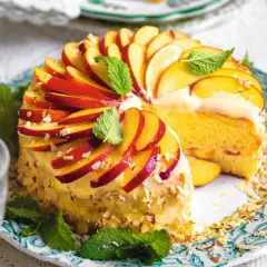 Torta di pesche morbidissima, decorata con fettine di pesca, mandorle e menta. Un dolce estivo invitante.