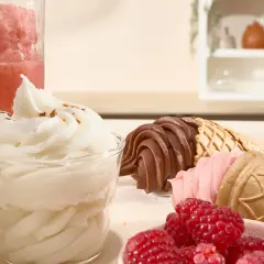 Un bicchiere di gelato sorbetto bianco, coni con gelato al cioccolato e fragola, lamponi freschi e una granita rosa.