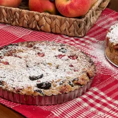 Una torta putana, ricca di frutta e spolverata di zucchero a velo, su una tovaglia a quadri rossi.