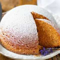 Torta Camilla ricetta originale: soffice torta cosparsa di zucchero a velo, con una fetta tagliata che rivela l'interno dorato e profumato.