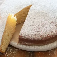 Torta soffice senza uova, cosparsa di zucchero a velo, con una fetta tagliata che ne mostra l'interno dorato.