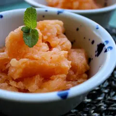 Sorbetto senza albume alla pesca, guarnito con menta fresca, servito in una ciotola decorata. Rinfrescante e leggero.