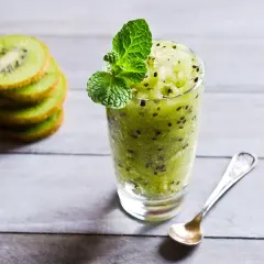 Sorbetto al kiwi rinfrescante, guarnito con menta, accanto a fette di kiwi impilate e un cucchiaino.