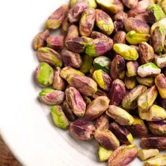 Pistacchi sgusciati su un piatto bianco, un assaggio di dove cresce il pistacchio in Italia, con i loro colori verdi e viola.
