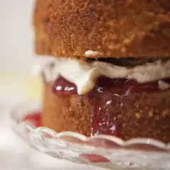 Torta soffice con panna e tanta marmellata di fragole che cola, servita su un piatto di cristallo.