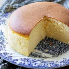 Una soffice torta giapponese, dorata in superficie e chiara all'interno, servita su un piatto decorato con un paesaggio in stile antico.
