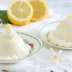 Deliziose delizie al limone, dolci cremosi su piattini fioriti, guarniti con panna e scorza di limone.