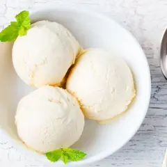 Tre palline di gelato alla vaniglia in una ciotola bianca, guarnite con menta. Perfetto per scoprire come rendere cremoso il gelato fatto in casa.