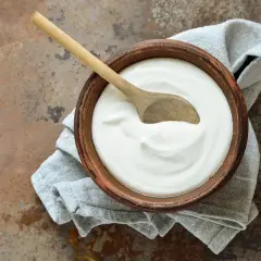 Ciotola di terracotta con panna fresca e cucchiaio di legno, un'idea su come si fa la panna da cucina in casa.