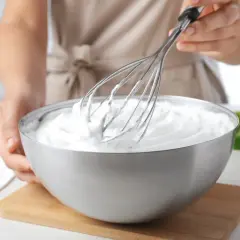Mani che montano panna in una ciotola d'acciaio con frusta. Ecco come fare se la panna non si monta.