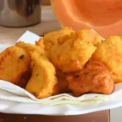 Frittelle di zucca dorate e croccanti, servite su carta assorbente, con una fetta di zucca sullo sfondo.