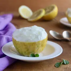 Sorbetto al limone ricetta: un fresco dessert servito in un limone svuotato, con limoni affettati e menta sullo sfondo.