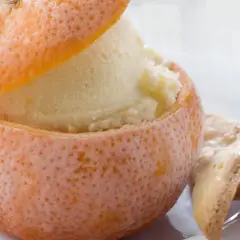Sorbetto all'arancia servito in una scorza d'arancia ghiacciata, accompagnato da biscotti croccanti.