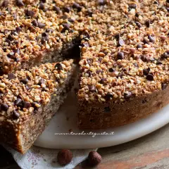 Deliziosa torta di nocciole piemontese, ricca di nocciole tritate e gocce di cioccolato, con una fetta tagliata.