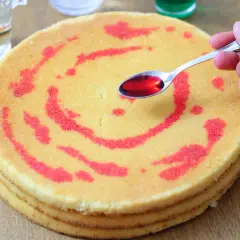 Un cucchiaino di sciroppo rosso viene versato su un pan di spagna a strati, decorato con un motivo a spirale.