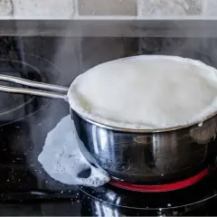 Latte che bolle in una pentola su un piano cottura a induzione, un esempio di come pastorizzare il latte in casa.