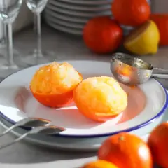 Sorbetto al mandarino senza gelatiera servito in coppette di mandarino. Frutta fresca e cucchiaio da gelato sullo sfondo.