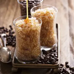 Due bicchieri di granita al caffè, con sciroppo che cola su uno. Chicchi di caffè tostati e cucchiaini completano la scena.