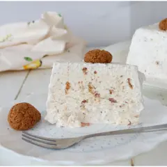 Una fetta di semifreddo agli amaretti, guarnita con un amaretto intero e un altro sul dolce intero sullo sfondo.