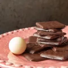 Piatto rosa con cioccolatini quadrati al cioccolato fondente e una pallina bianca. Un invito al gusto after eight.