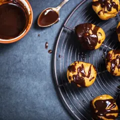 Profitterol ricetta: bignè dorati glassati con cioccolato fuso, pronti per essere gustati.