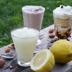 Tre granite siciliane, una al limone, preparate con gelatiera, su un tavolo di legno con limoni e mandorle.