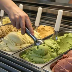 Mano che preleva il primo gusto di gelato inventato, un cremoso pistacchio, da una vaschetta piena di delizie.