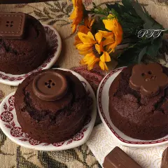 Tre deliziosi cupcake al cioccolato, decorati con bottoni di cioccolato, su piattini con fiori gialli sullo sfondo.