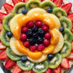 Torta alla frutta coloratissima, con fragole, kiwi, mandarini, lamponi e mirtilli disposti a raggiera su una base croccante.