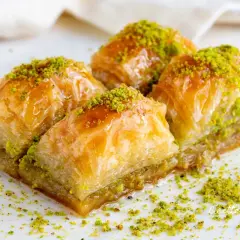 Quattro dolcetti di baklava, ricoperti di sciroppo dorato e pistacchi tritati, pronti per essere gustati.