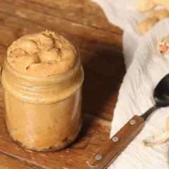 Barattolo di burro di arachidi fatto in casa, pronto per la tua prossima ricetta. Arachidi e cucchiaio su sfondo rustico.