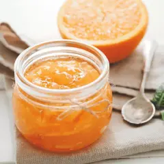 Barattolo di marmellata di arance fatto in casa, con una fetta d'arancia sullo sfondo.
