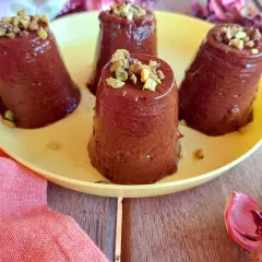 Quattro budini cachi e cacao, guarniti con pistacchi tritati, su un piatto giallo.
