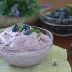 Delizioso gelato ai mirtilli fatto in casa con gelatiera, guarnito con mirtilli freschi e menta.