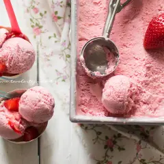 Coppette e vaschetta piene di cremoso gelato alla fragola, con fragole fresche e un cucchiaio pronto per servire.